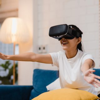 Asian teenager woman using glasses virtual reality simulator playing video games in living room, female feeling happy using relax time lying on sofa at home. Lifestyle women relax at home concept.