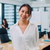 Portrait of successful beautiful executive businesswoman smart casual wear looking at camera and smiling in modern office workplace. Young Asia lady standing in contemporary meeting room.